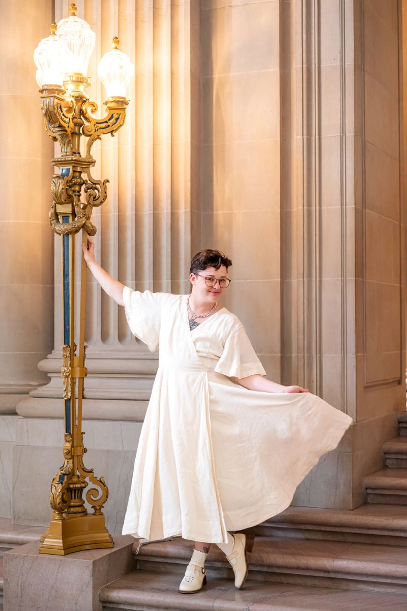 a person wearing a linen white dress standing next to a lampost 