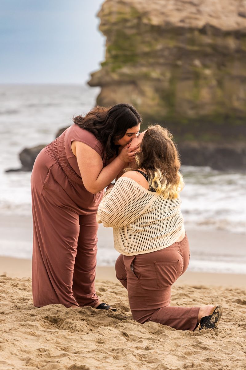 a couple kissing after one partner proposed to the other next to the ocean in santa cruz at natural bridges 