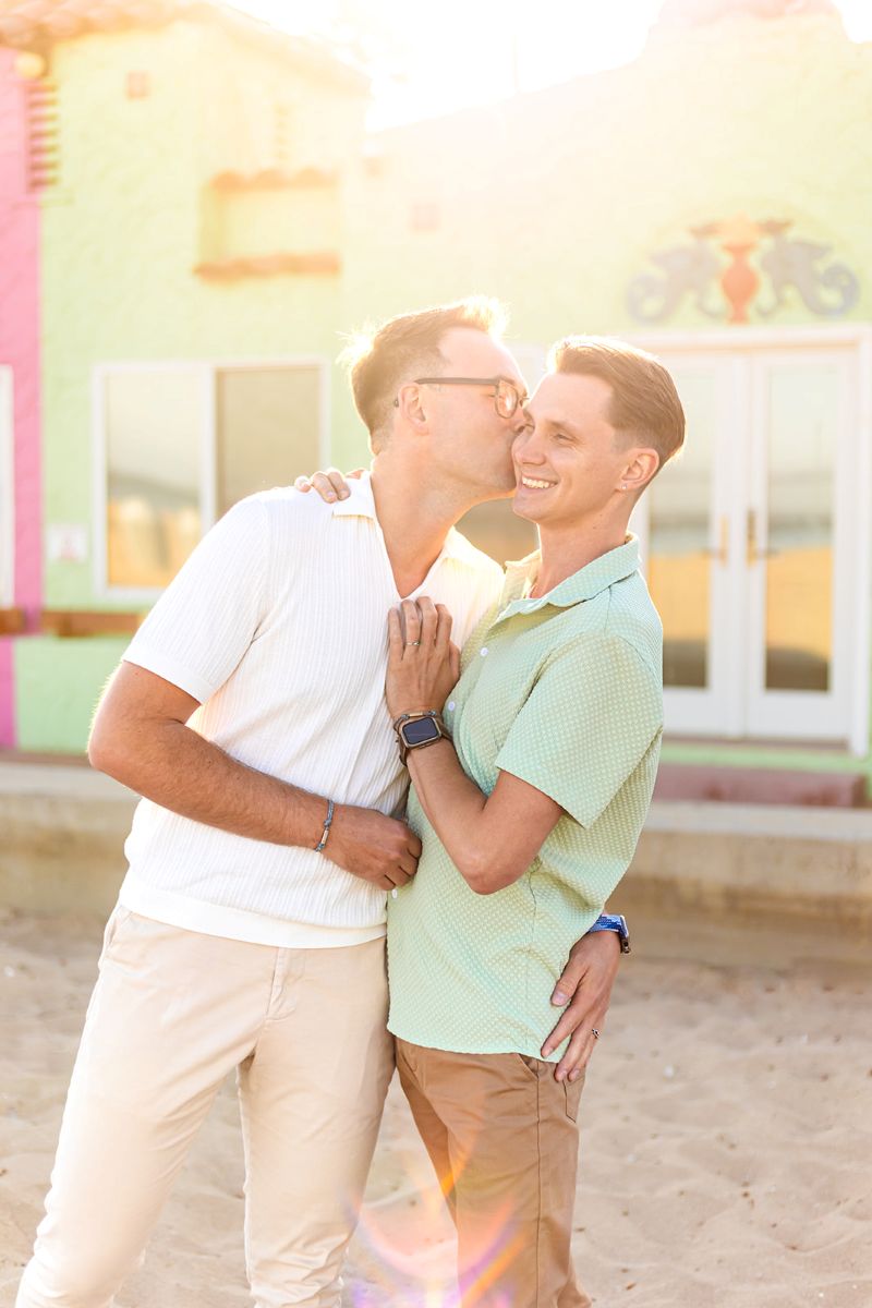 a man kissing his partner on the cheek and hugging him at capitola beach 