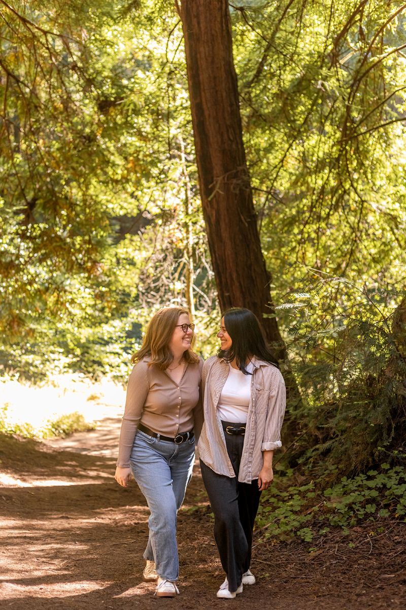 a couple walking hand in hand down a trail laughing with each other in henry cowell state park 