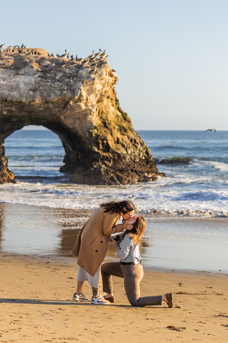 a surprise proposal happening at natural bridges in santa cruz on the beach next to the water 