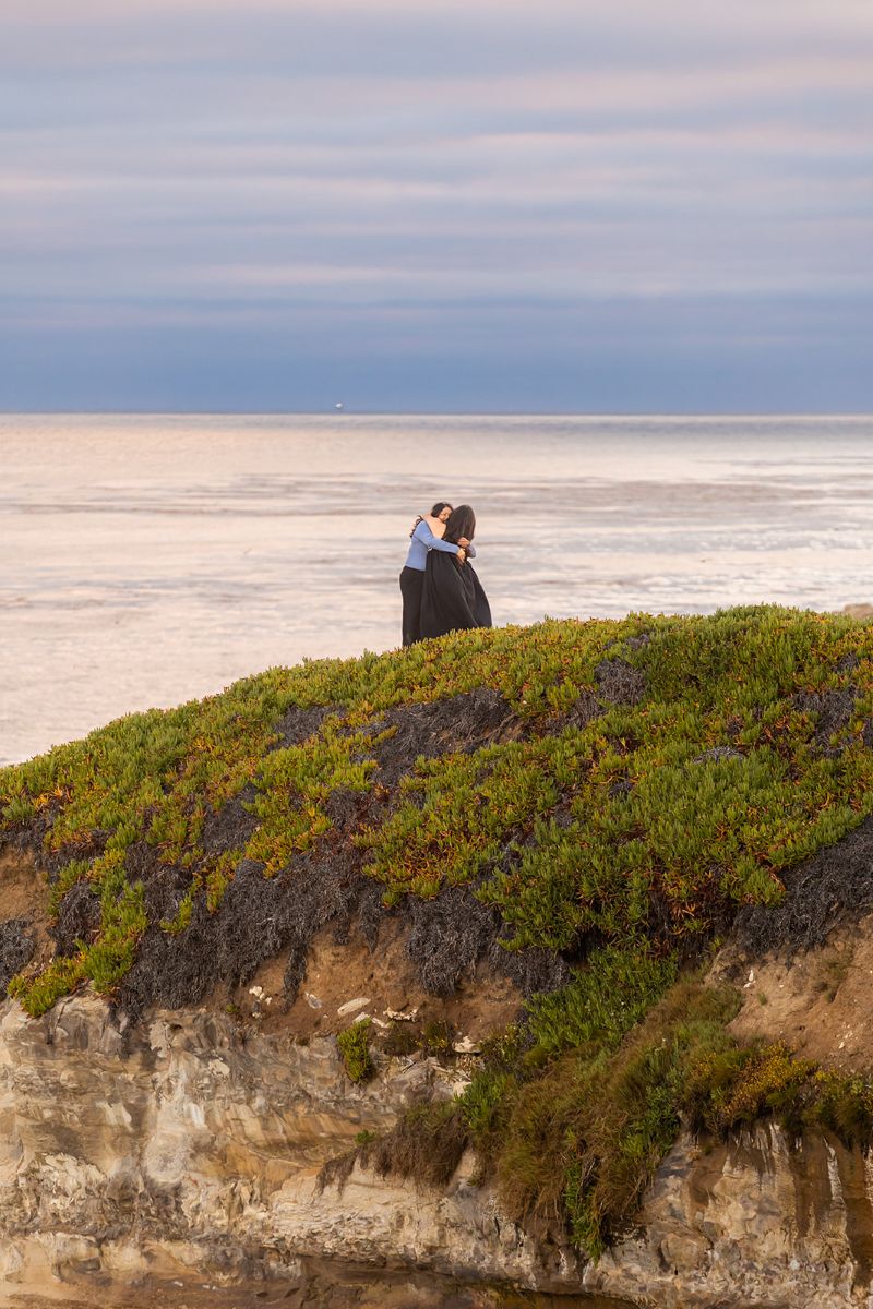 a couple embracing on the cliffside of west cliff drive next to the water