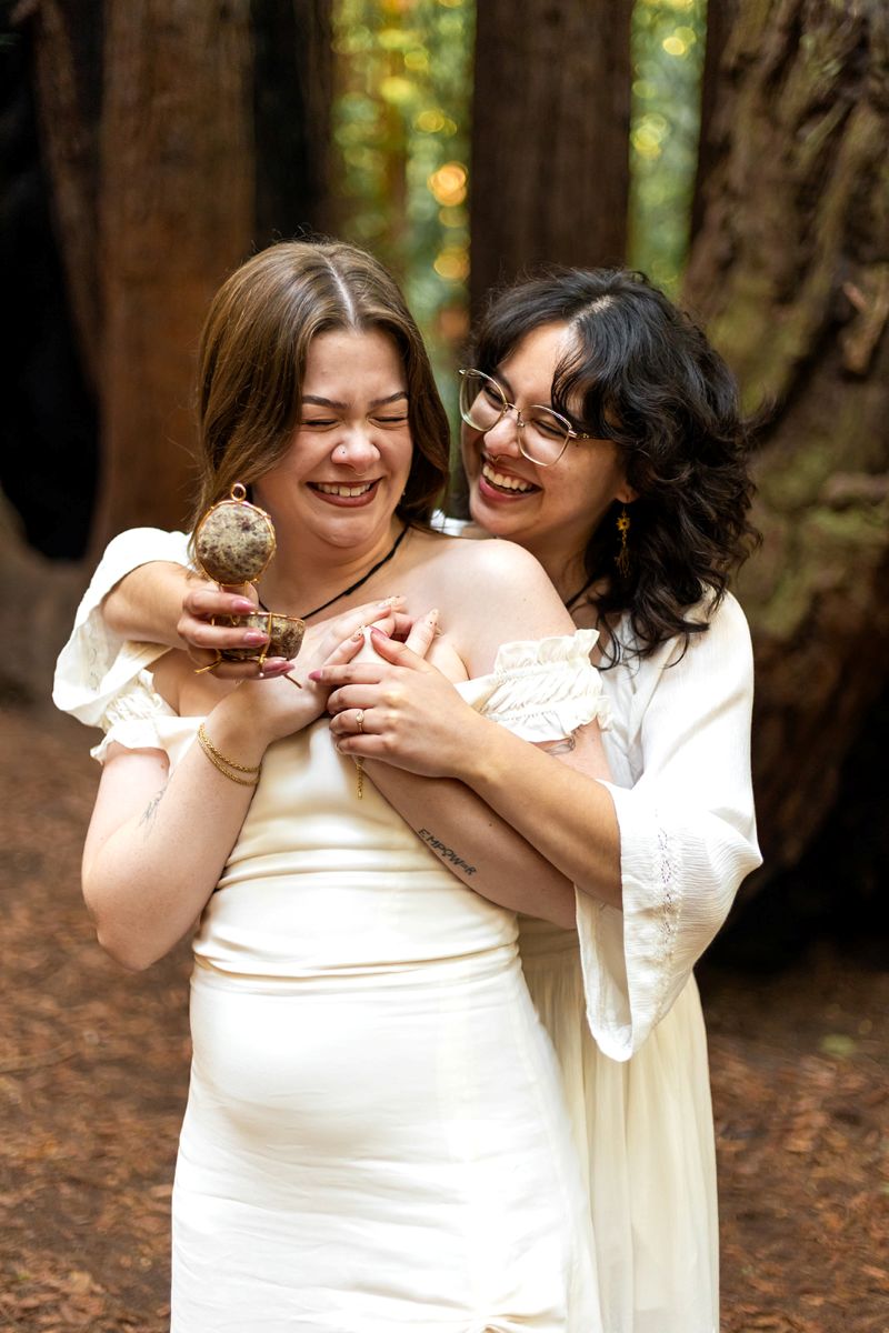 a woman proposing to her partner in henry cowell state park and she is hugging her from behind 