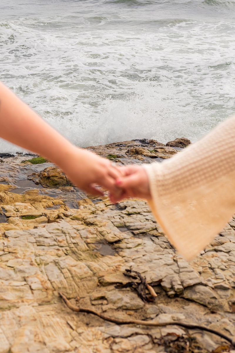 a couple holding hands on a rock at natural bridges next to the oceans 