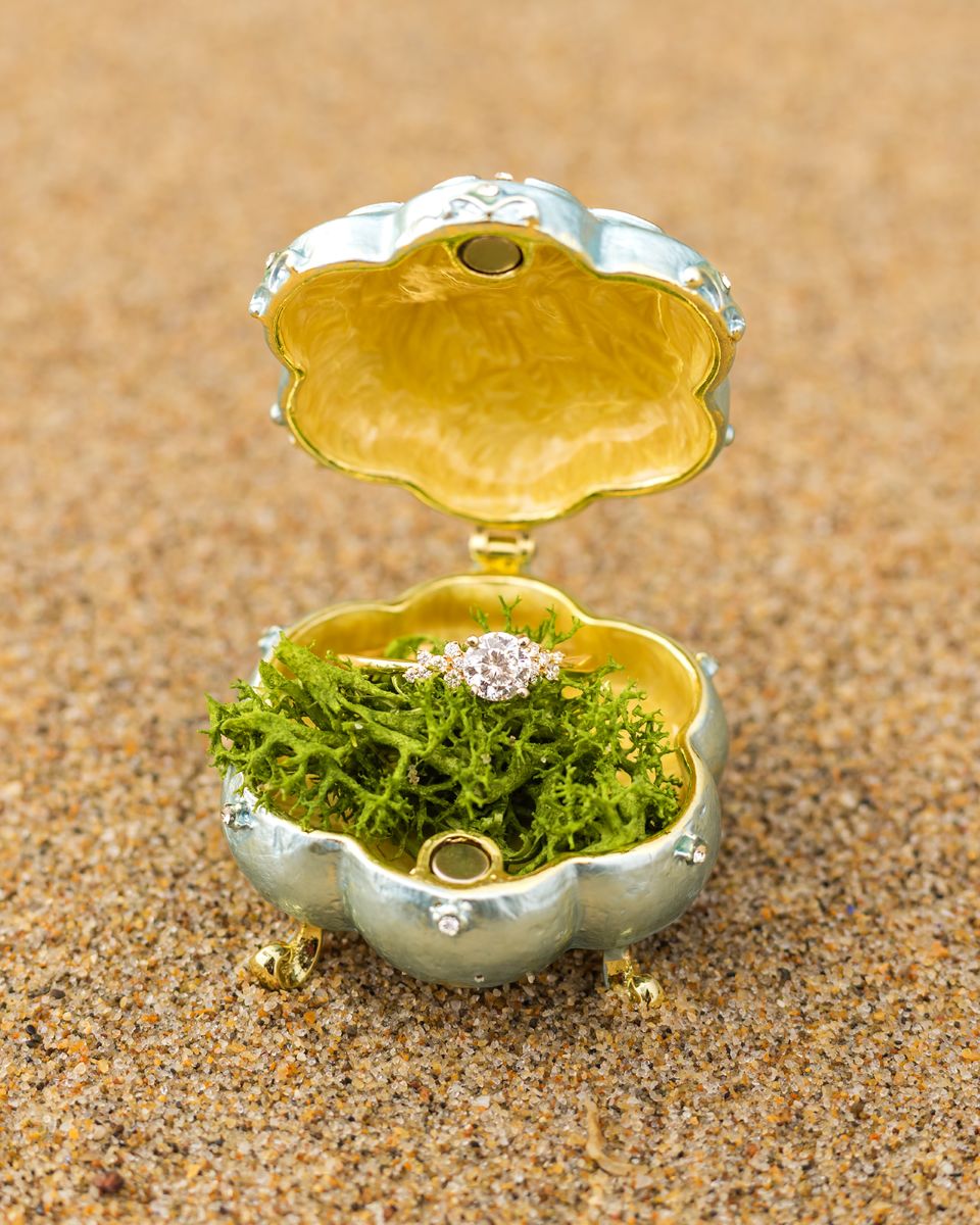 an elegant ring box with moss and a diamond ring inside on the sand 