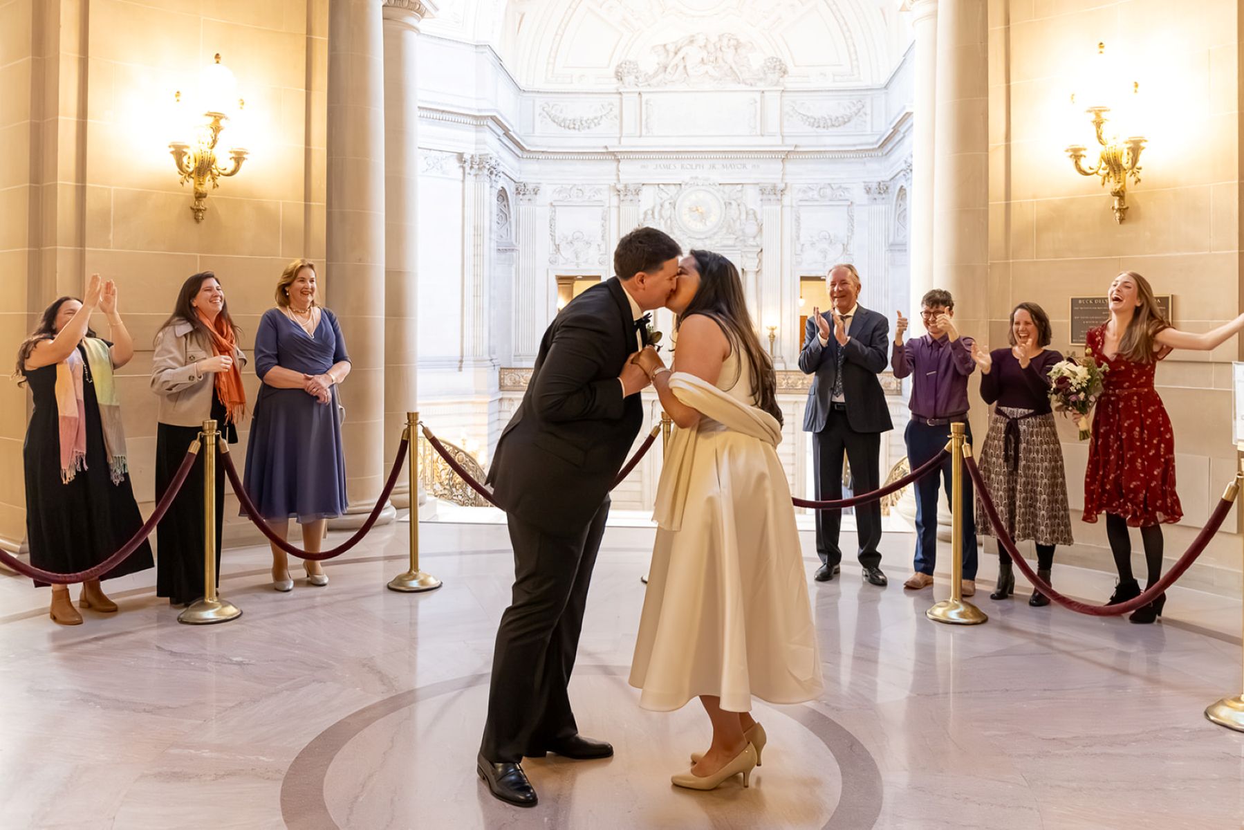 a couple having their wedding ceremony in san francisco city hall they are both kissing each other while their guests cheer for them