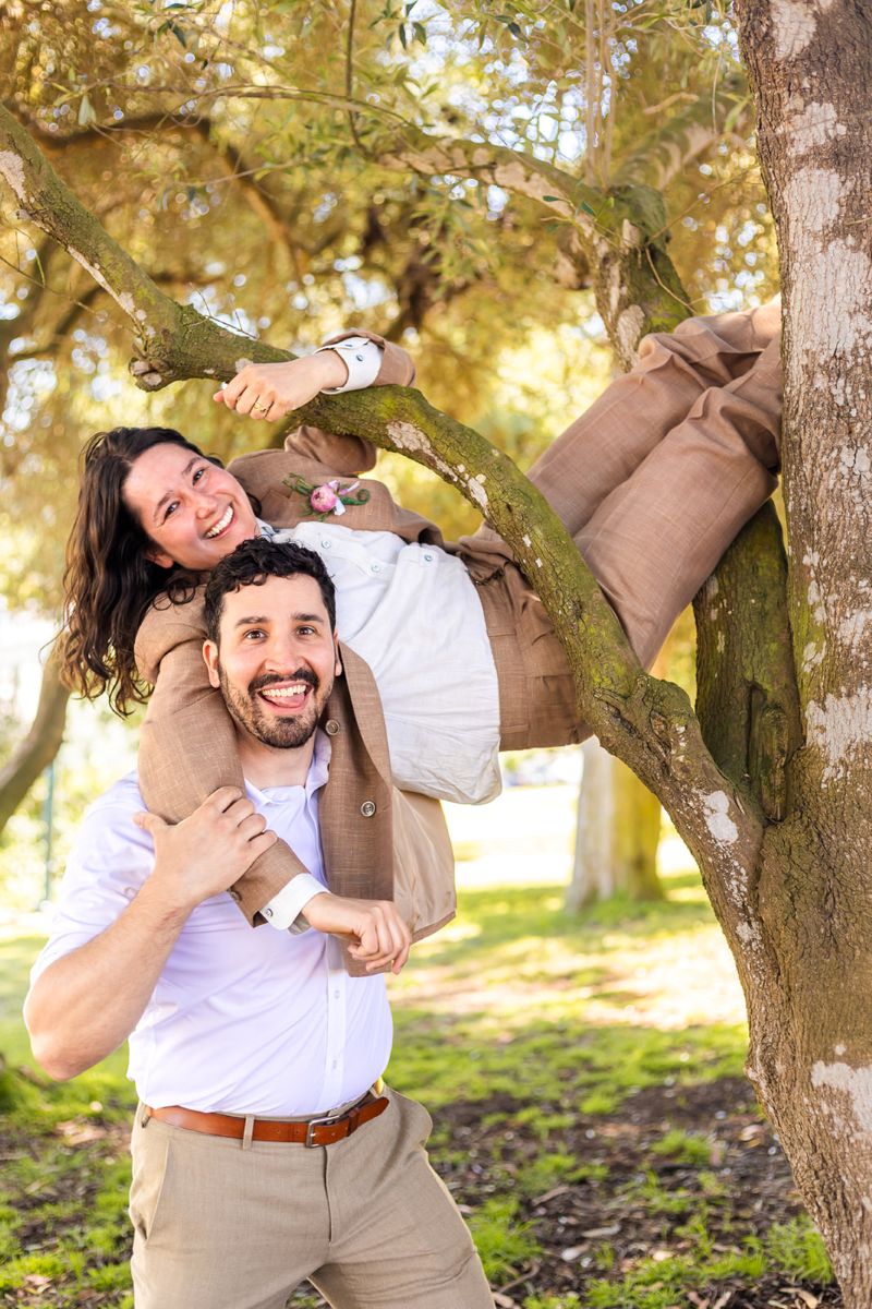 a person in a tree wrapping their arms around a person who is standing next to them underneath the tree