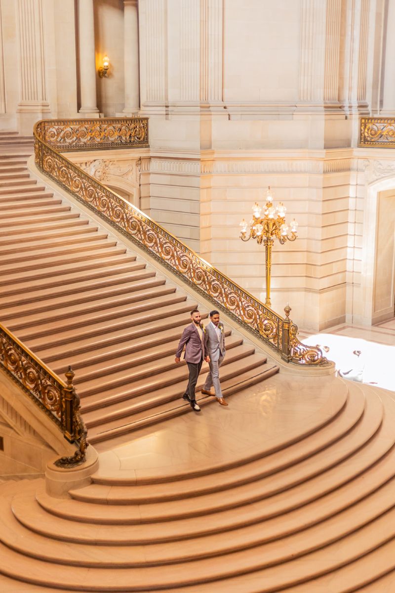 a couple walking hand in hand down the stairs in san francisco city hall