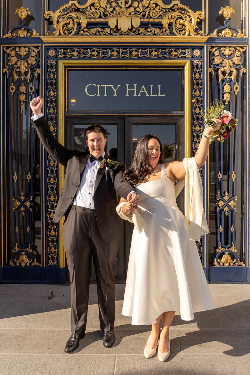 a couple outside of san francisco city hall taking wedding portraits after their wedding ceremony
