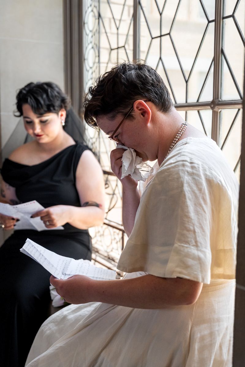 a couple sitting together on a wedding sill reading personalized wedding vows they wrote for each other