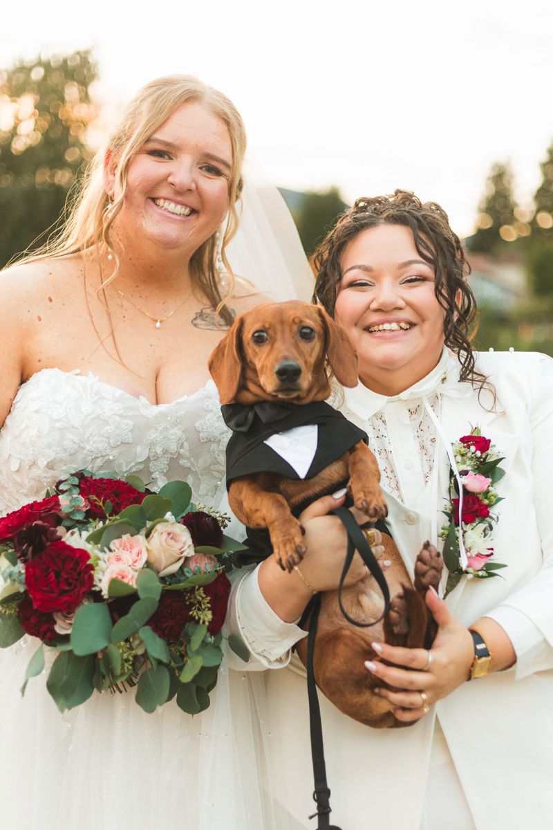 two brides smiling and holding their dog
