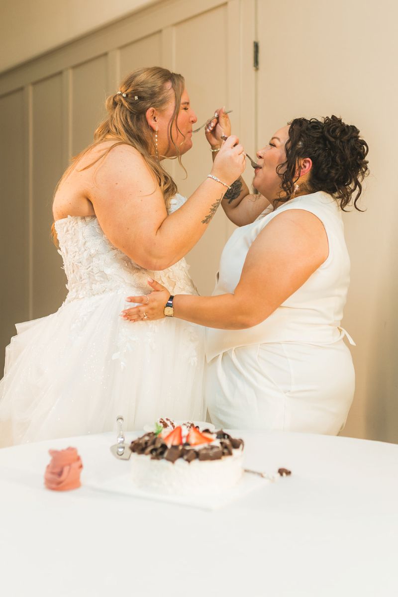 two brides feeding each other wedding cake at their wedding reception