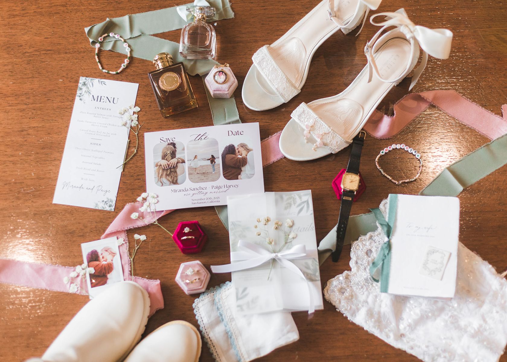 a wedding detail flat lay with wedding invitations, a watch, wedding rings, polaroids, boots, and ribbons