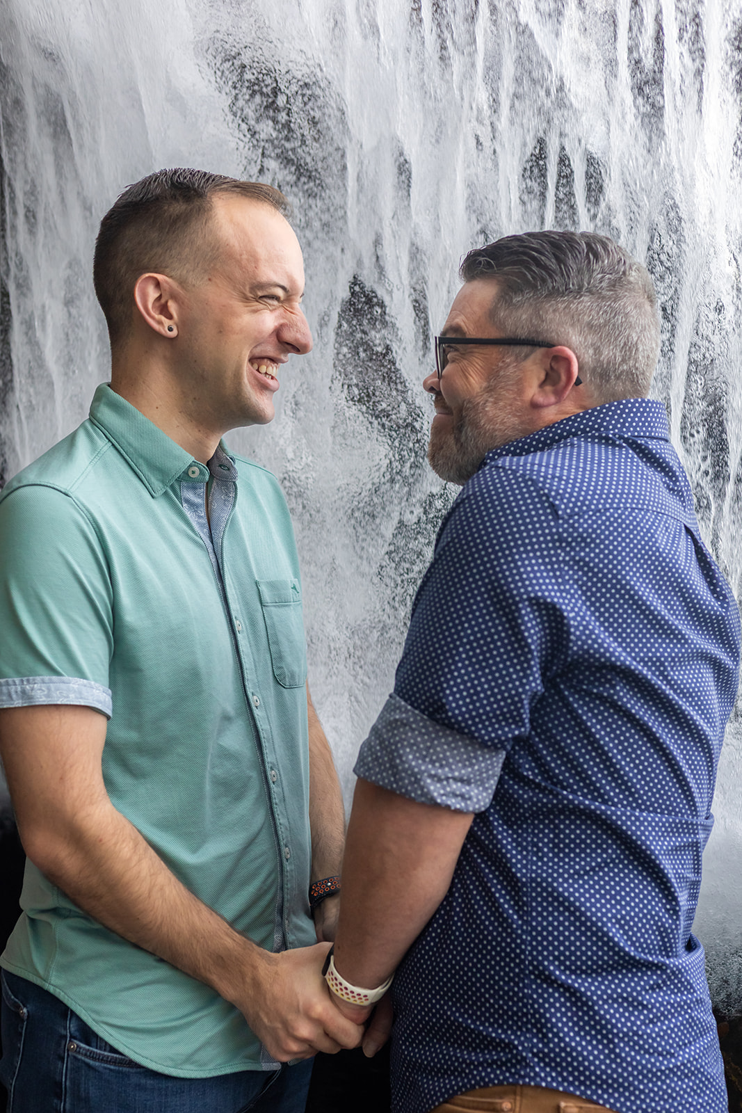 a queer couple holding hands and standing next to a waterfall inside of monterey bay aquarium 