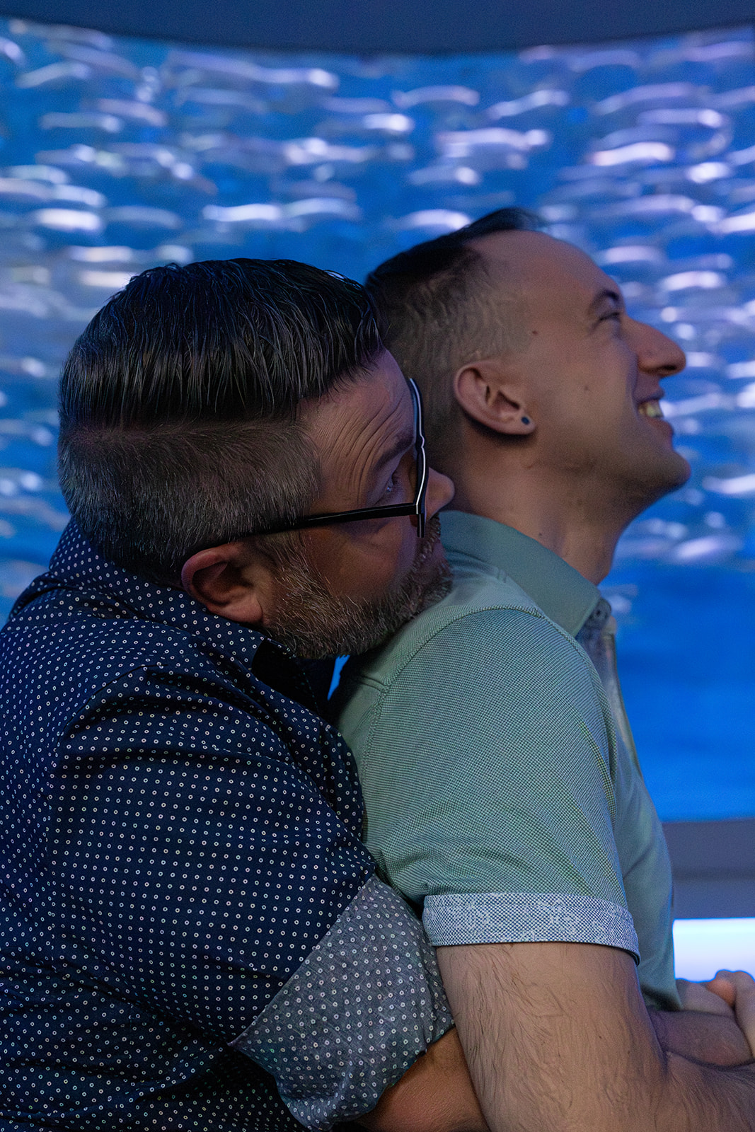 a man hugging his partner from behind as they both watch the fish swim by inside the monterey bay aquarium 